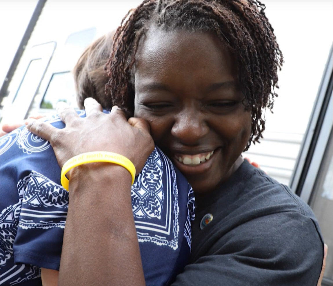 Hummingly in action after disaster. Two people hugging outdoors, one wearing a yellow bracelet.